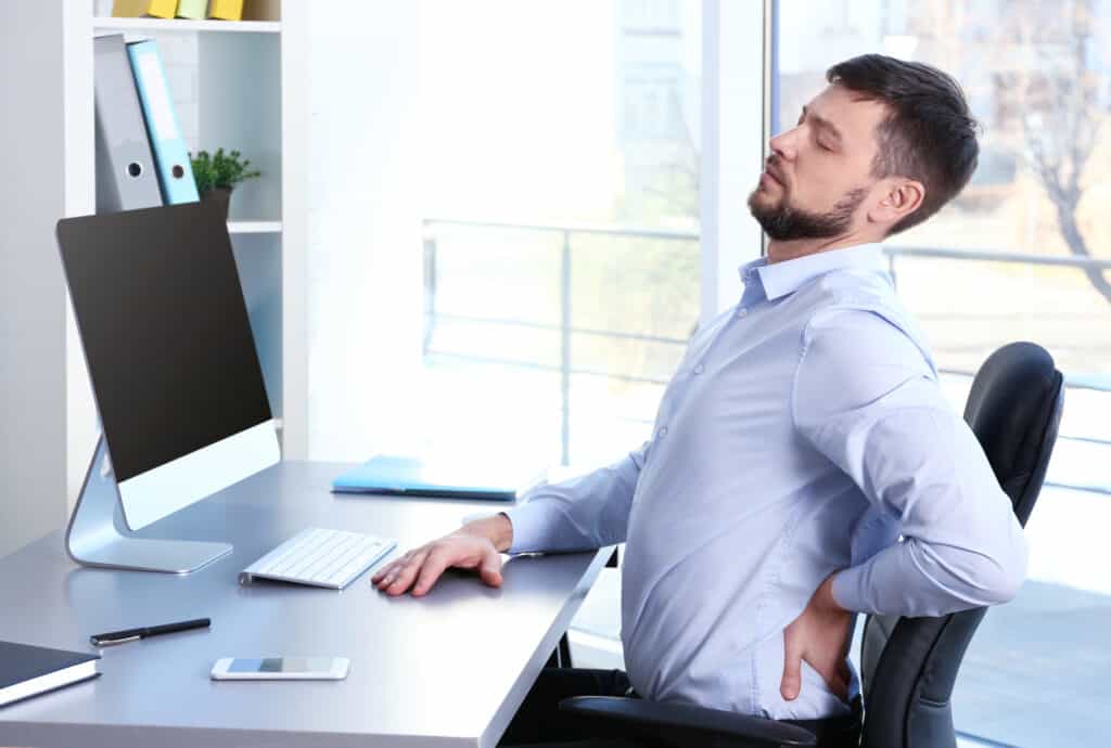 Posture concept. Man suffering from back pain while working with computer at office