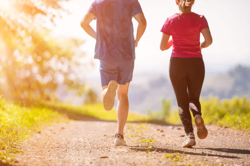 young happy couple enjoying in a healthy lifestyle while jogging on a country road through the beautiful sunny forest, exercise and fitness concept