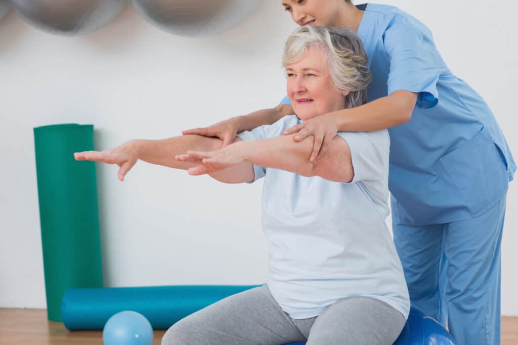 Instructor assisting senior woman to exercise in gym